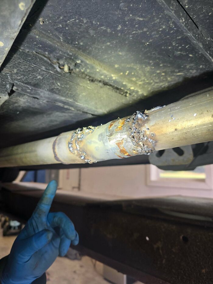 A car mechanic pointing at a poorly welded car exhaust pipe, dealing with a repair.