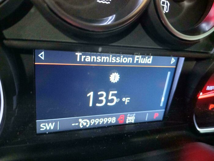 A car mechanic monitoring transmission fluid temperature on a car's dashboard, dealing with diagnostics.