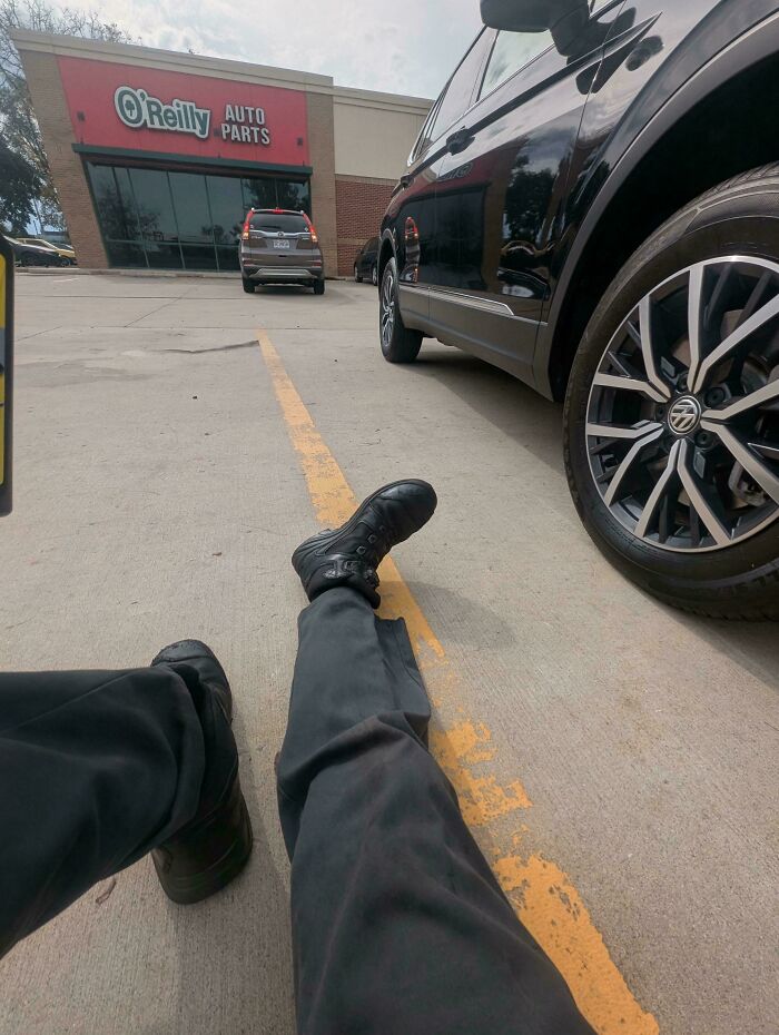 A car mechanic sitting on the ground next to a car at O'Reilly Auto Parts, dealing with a car issue.