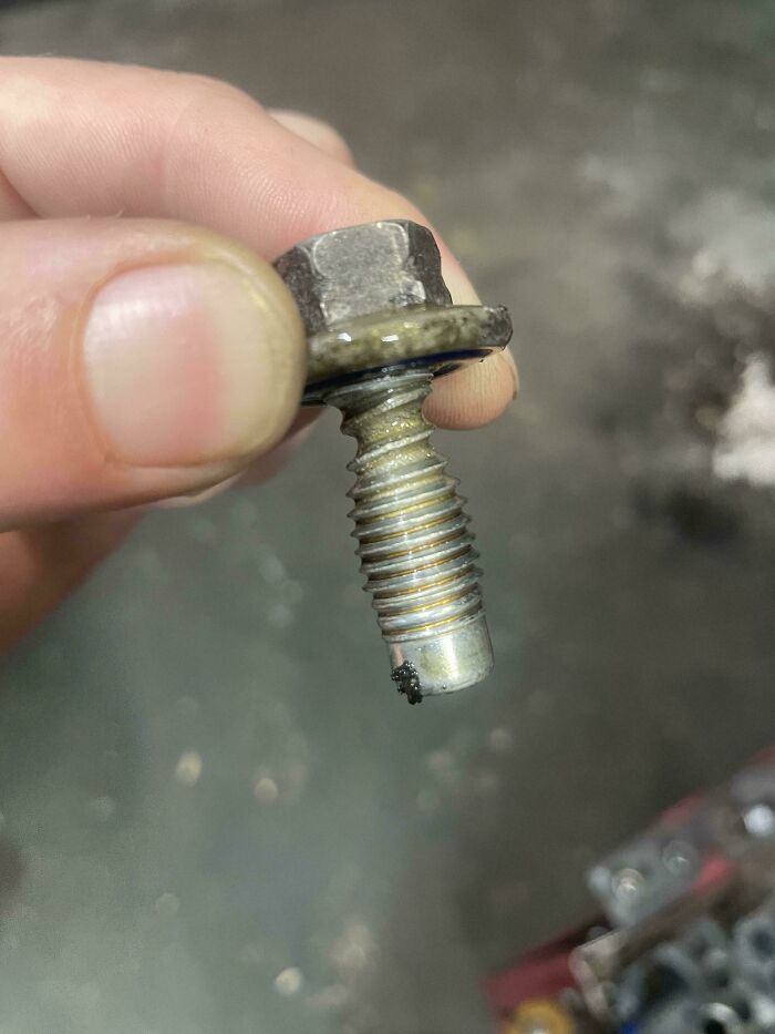 A close-up of a dirty, partially stripped bolt held between two fingers, revealing issues car mechanics face.