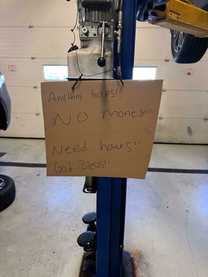 A handwritten sign by car mechanics in a shop reads Anything helps!! NO money!! Need hours!! God Bless!!