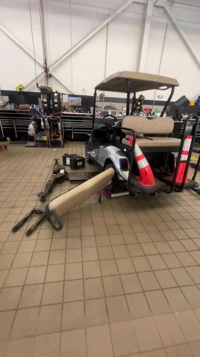Car mechanics working on a golf cart with removed seats and parts in the garage.