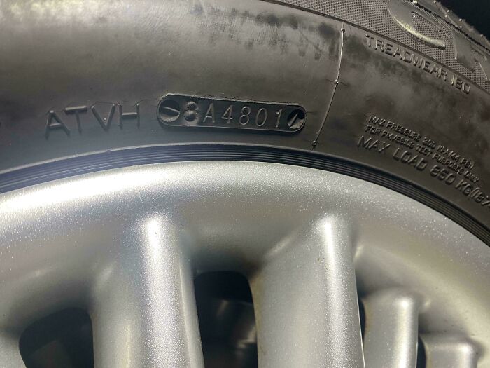 Car mechanics inspect a tire with visible manufacturing date and tread wear, for maintenance.