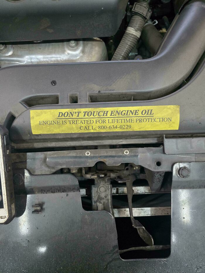 A close-up of a car engine with a warning sticker about engine oil, something car mechanics frequently encounter.