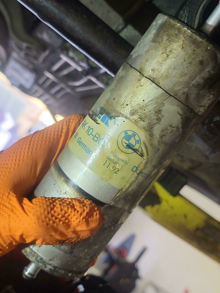 A car mechanic holding a dirty BMW fuel filter, showing the car mechanics are dealing with old car parts.