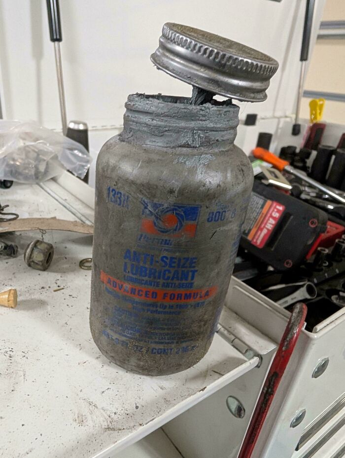 Car mechanics encounter an old, used container of anti-seize lubricant, highlighting tools used in car repair.
