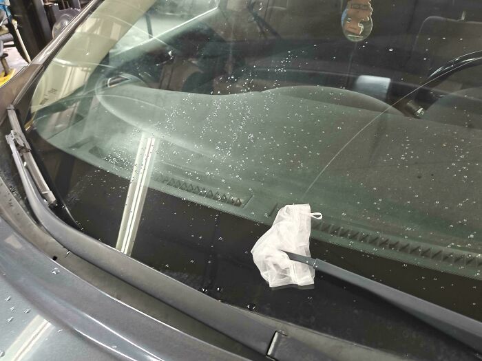 A car windshield covered in water droplets with a small white bag on the wiper, an odd sight for car mechanics.