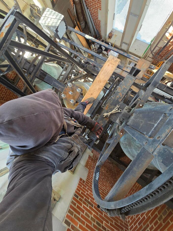 A car mechanic working high up amidst metal structures, possibly a bell tower, showcasing challenging repairs.
