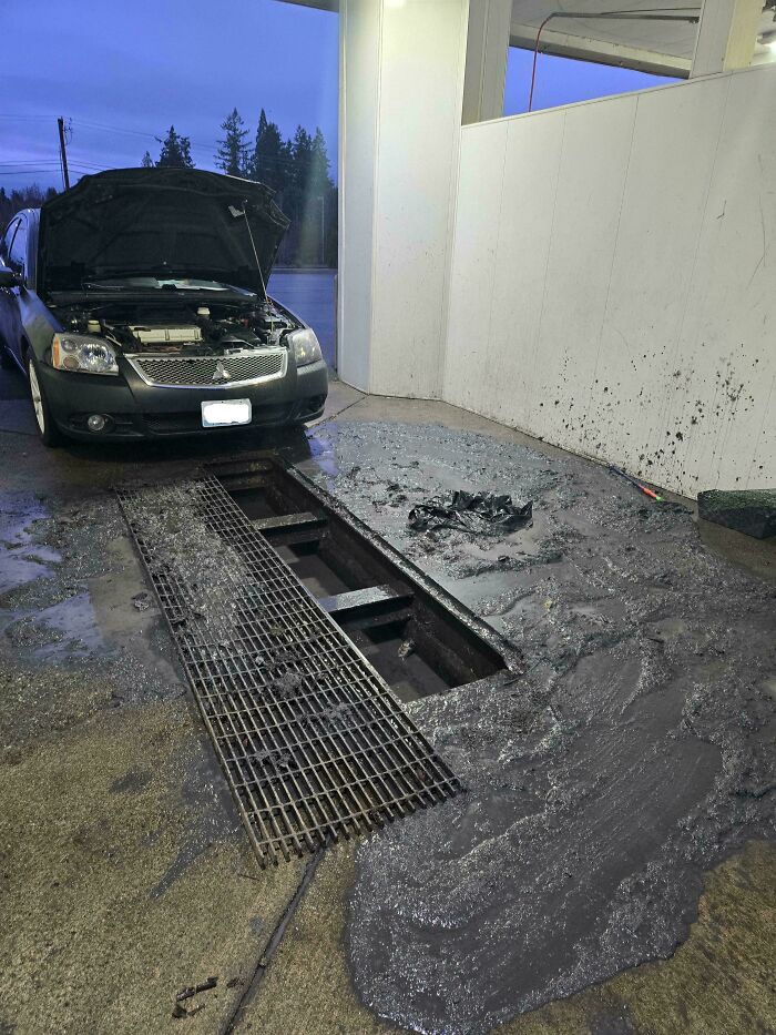 A car with its hood open, parked over a large pool of dark mud, illustrating a messy car mechanics job.