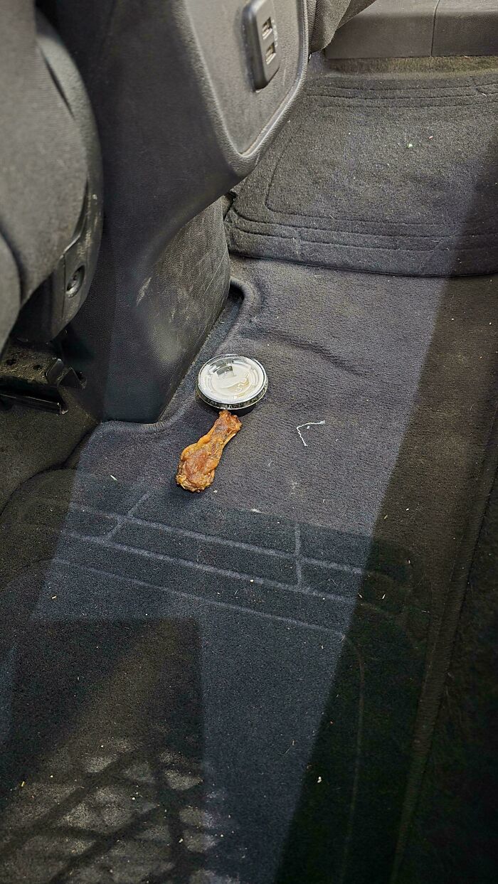 A gnawed chicken bone and a cup lid on a dirty car floor, revealing odd things car mechanics encounter.