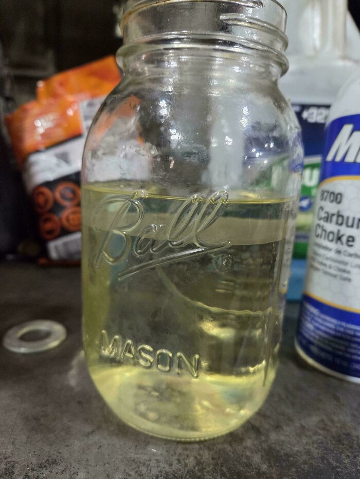 A mason jar filled with a yellow liquid, possibly a car fluid issue, for car mechanics to diagnose.