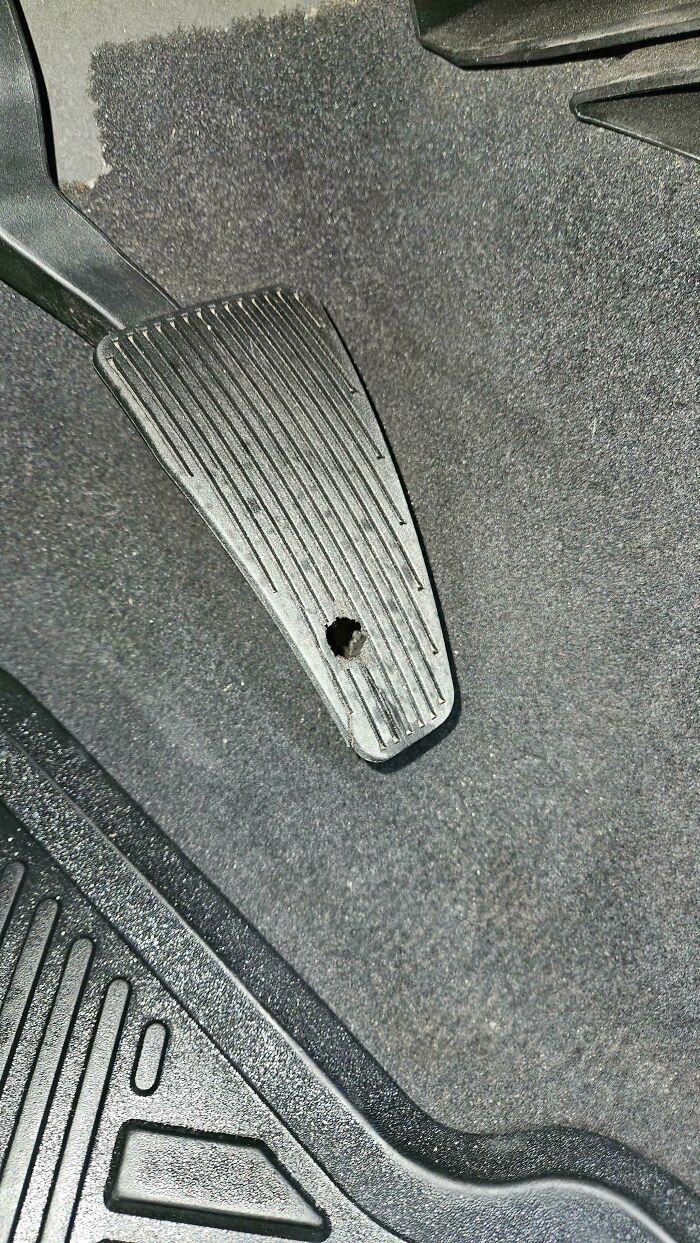 A car mechanic dealing with a worn-out car pedal, showing a hole worn through the rubber, requiring attention or replacement.