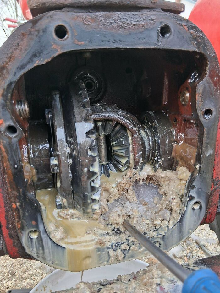 A car mechanic dealing with a severely damaged car differential, filled with sludge and debris, highlighting a challenging repair.