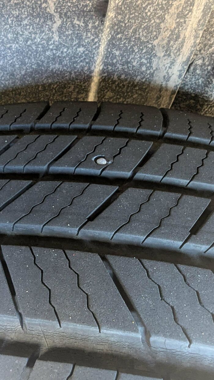 A close-up of a car tire with a large nail lodged in its tread, a common issue for car mechanics.