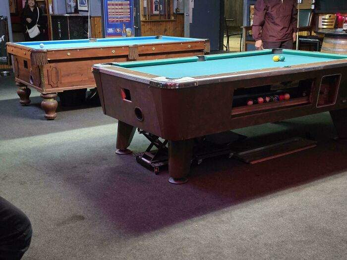 Two pool tables, one visibly propped up with a jack, showcasing unusual car mechanics related situations.