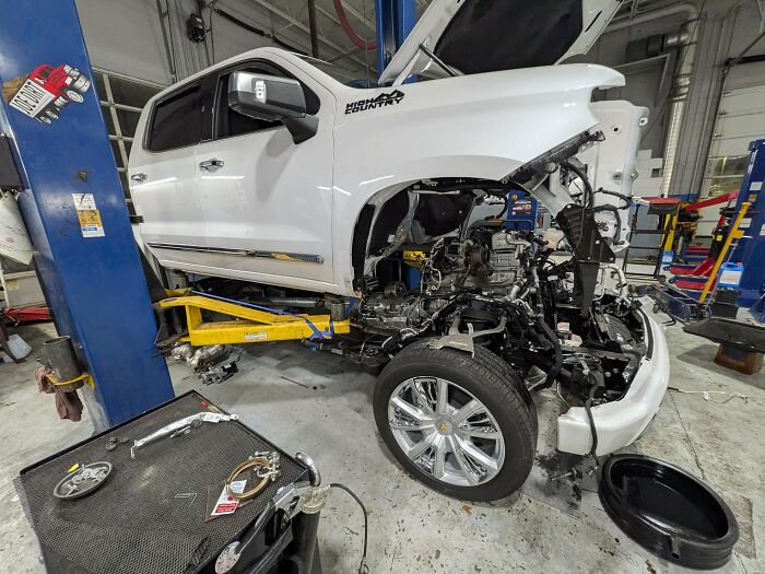 A car mechanic's work on a white pickup truck, with the front end disassembled in a garage.