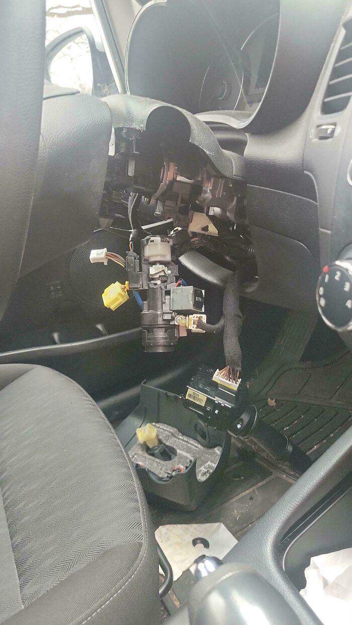 A car mechanic's view of a car's dashboard and steering column dismantled, revealing wires and components.