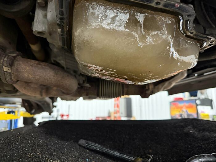 An underside view of a car engine with a pan full of ice, an unusual and challenging issue for car mechanics.