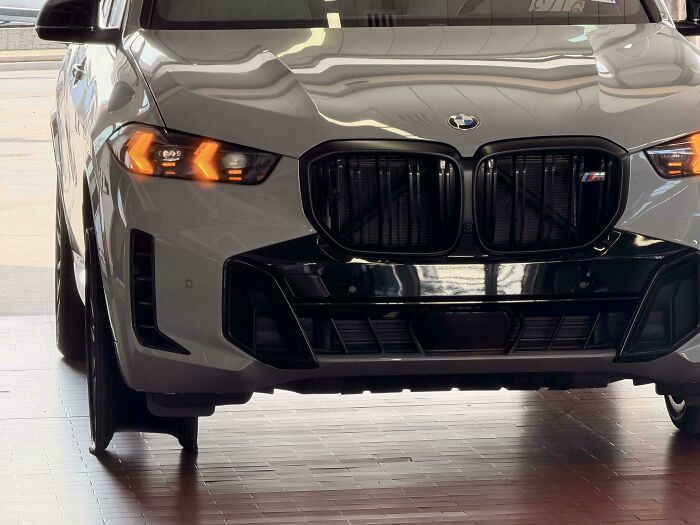 The front view of a modern white car with its headlights on, highlighting a new vehicle car mechanics work on.