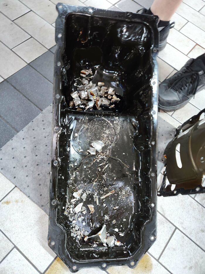 Car mechanics find metal shards in an oil pan, revealing significant engine damage.