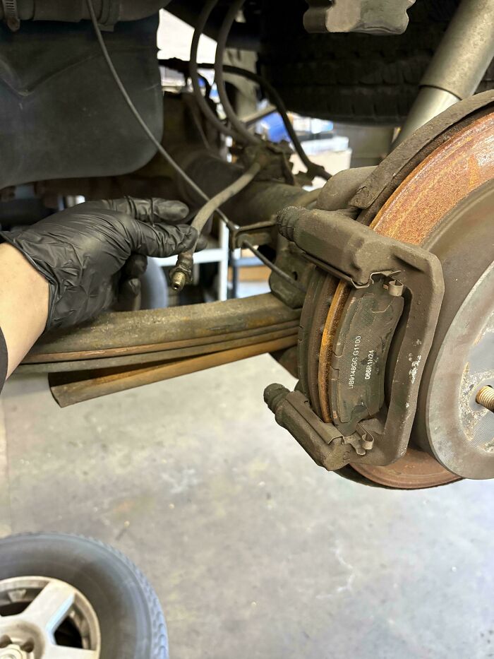 Car mechanics inspect a rusty brake rotor and caliper on a vehicle, indicating brake maintenance.