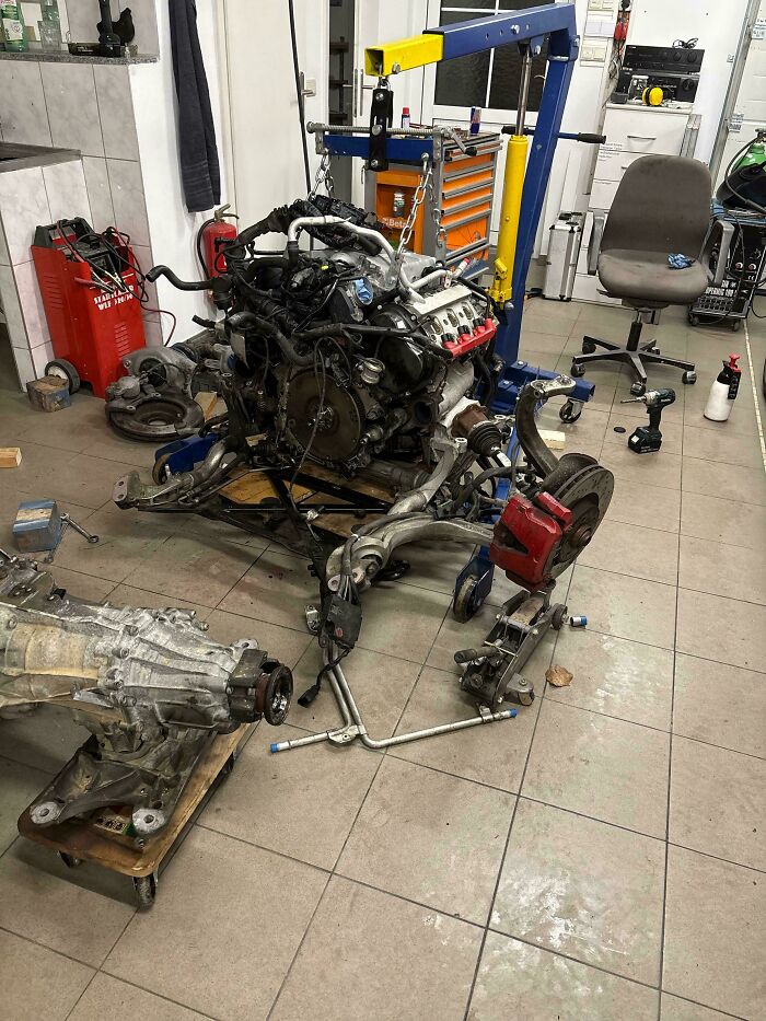 Car mechanics work on a completely disassembled engine, highlighting a complex automotive repair.