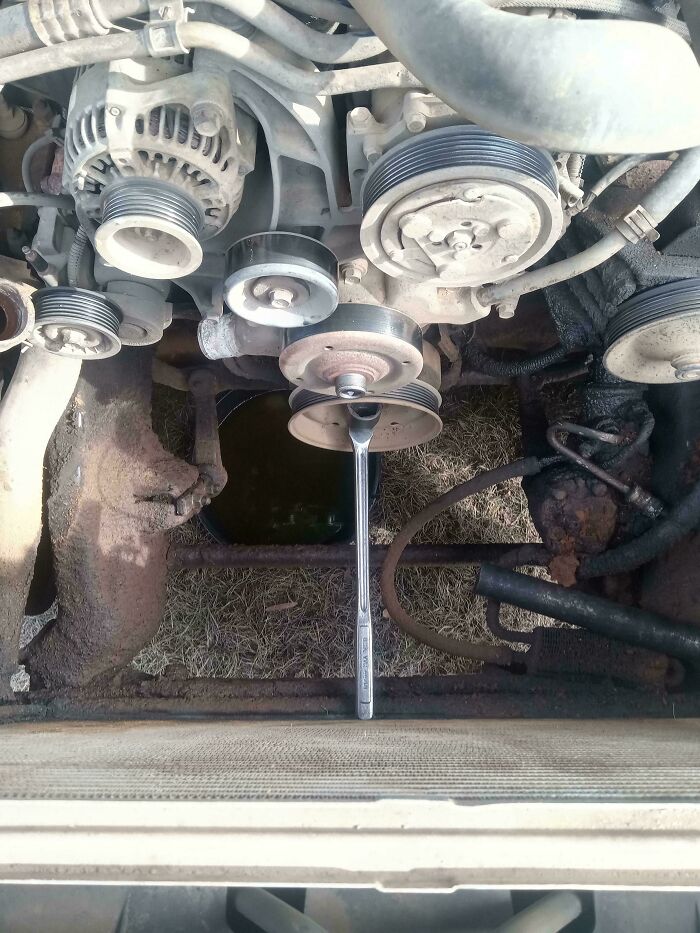 A car mechanic tool, a wrench, stuck upright in a dirty car engine compartment, a difficult repair.