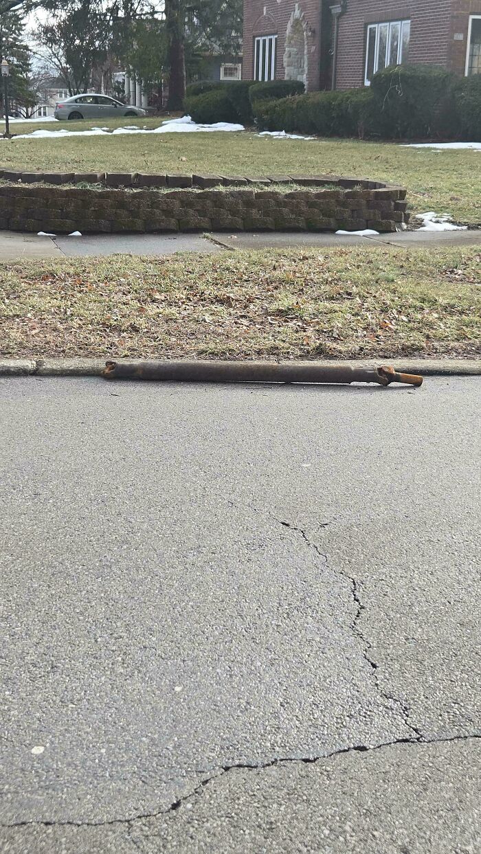Car mechanics notice a long, broken car part, likely a drive shaft, lying on the asphalt street.