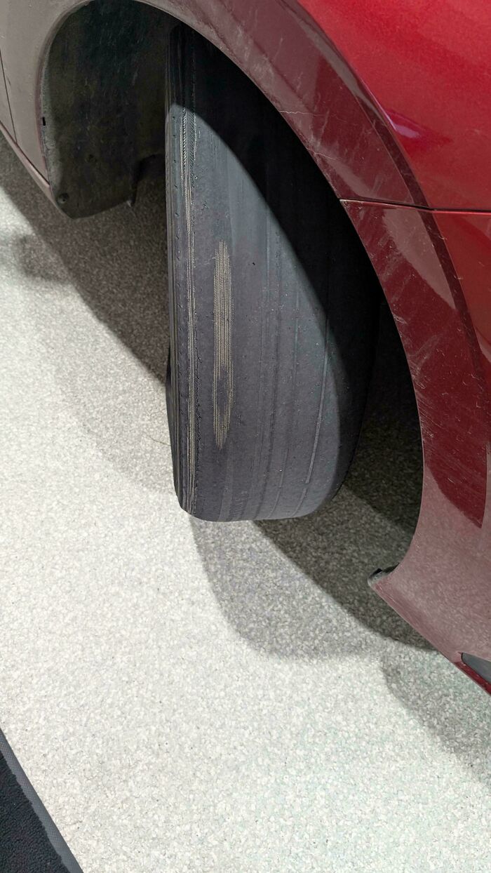 Car mechanics inspect a severely worn-out car tire, completely bald with visible internal cords, on a red car.