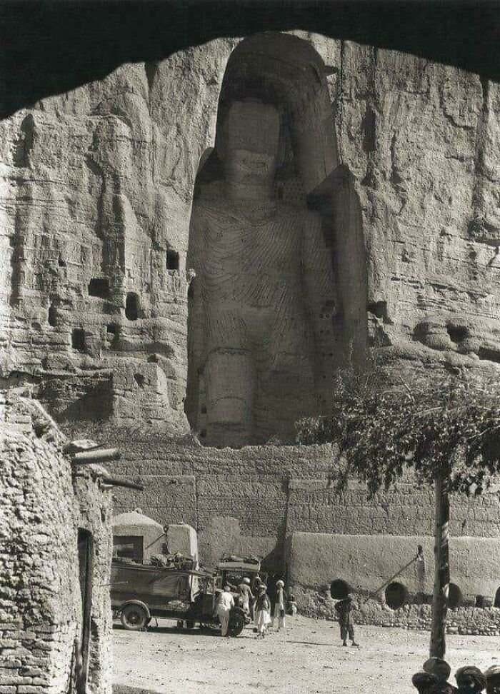 A striking historical photo capturing the immense, ancient Buddha statues carved into the Bamiyan cliffs.