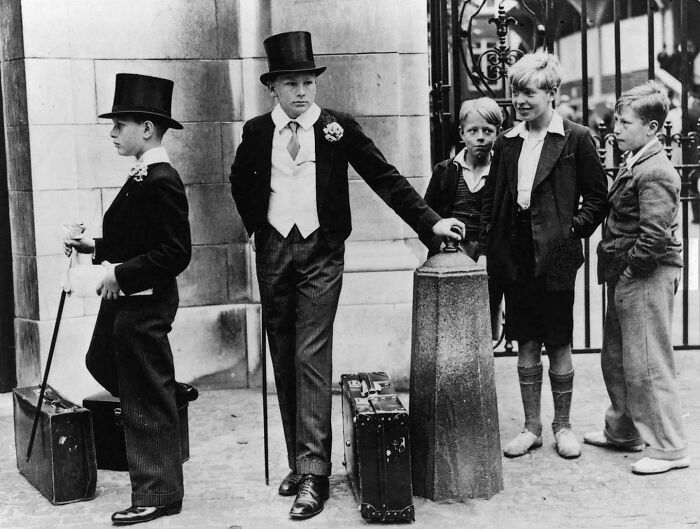 A fascinating historical photo showing young boys dressed in formal attire with top hats and suitcases, depicting days of travel.