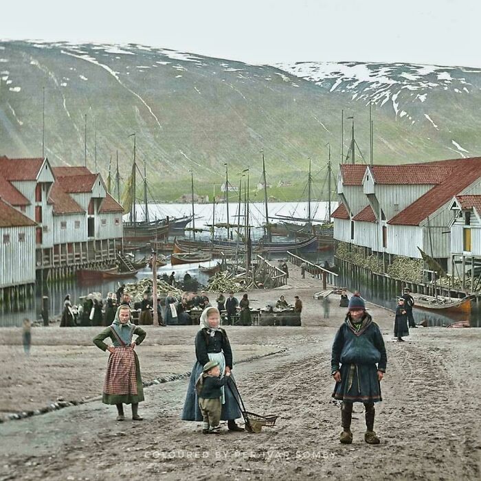 A vibrant historical photo of a village with boats docked in the background and people gathered on the shore, reminding us of days gone by.