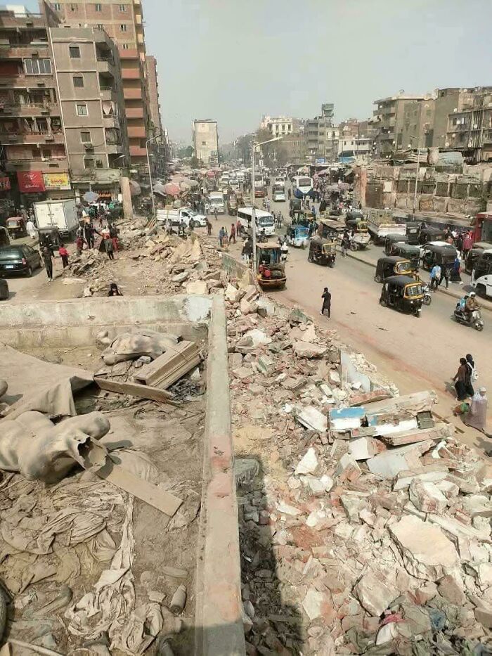 Chaotic urban street scene with rubble, damaged buildings, and heavy traffic in daylight