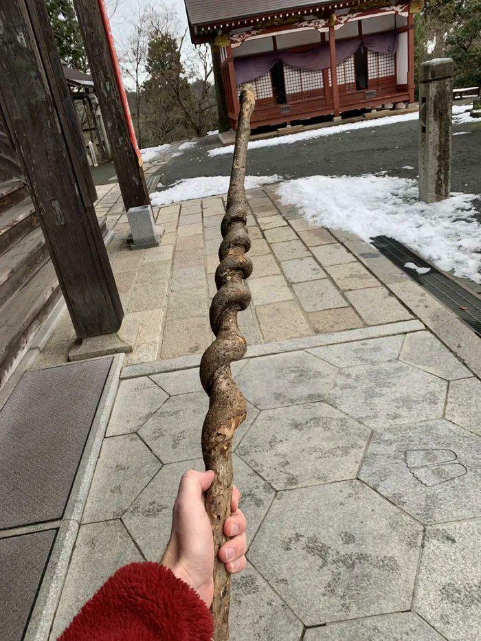 Person holding a cool twisted wooden stick outdoors near traditional buildings and patches of snow on the ground.