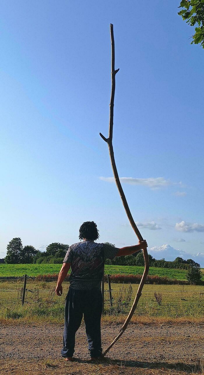 Person standing outdoors holding a very tall cool stick against a clear blue sky with greenery in the background.