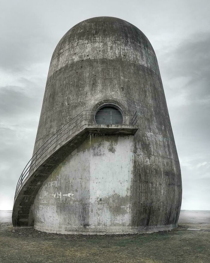 A towering, egg-shaped concrete building with a single round window and an external staircase, ideal for an evil mastermind.