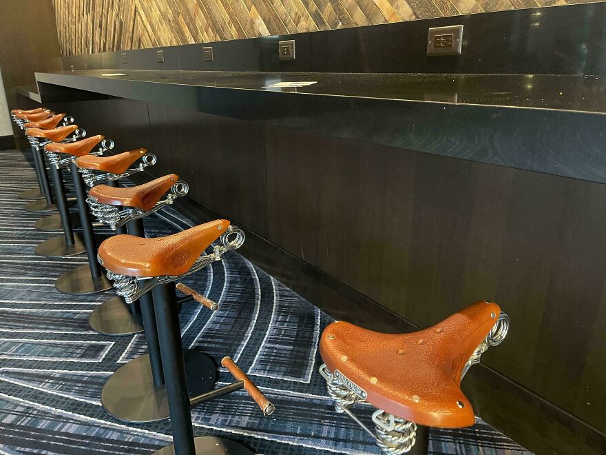 Row of stools with bicycle seats and footrests under a countertop with power outlets, showing designers went too far in usability.