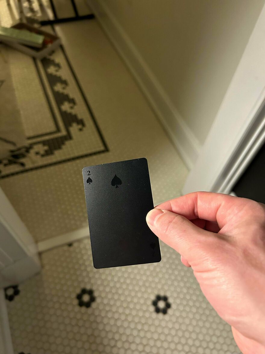 Hand holding a black playing card with barely visible details, showcasing a designer fail making things impossible to use.