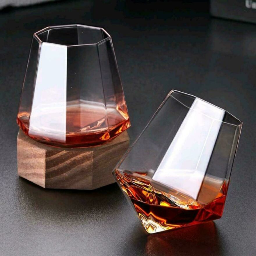 Two modern designer glasses with angled bases, one tipped over, showcasing a design that makes them difficult to use.