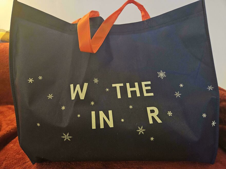 Black tote bag with orange handles featuring a confusing design missing letters, showcasing impossible to use designer creativity.