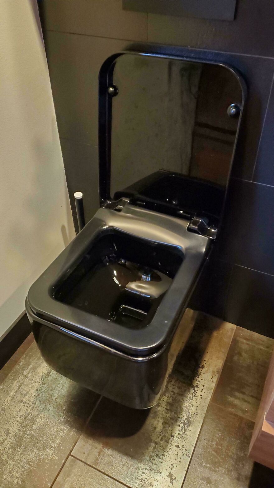 Black toilet with a square-shaped bowl and reflective lid, an example of designers going too far and making things impossible to use.