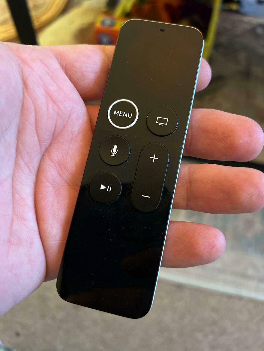 Hand holding a minimalist remote control with difficult-to-use button design in a poor lighting setting.