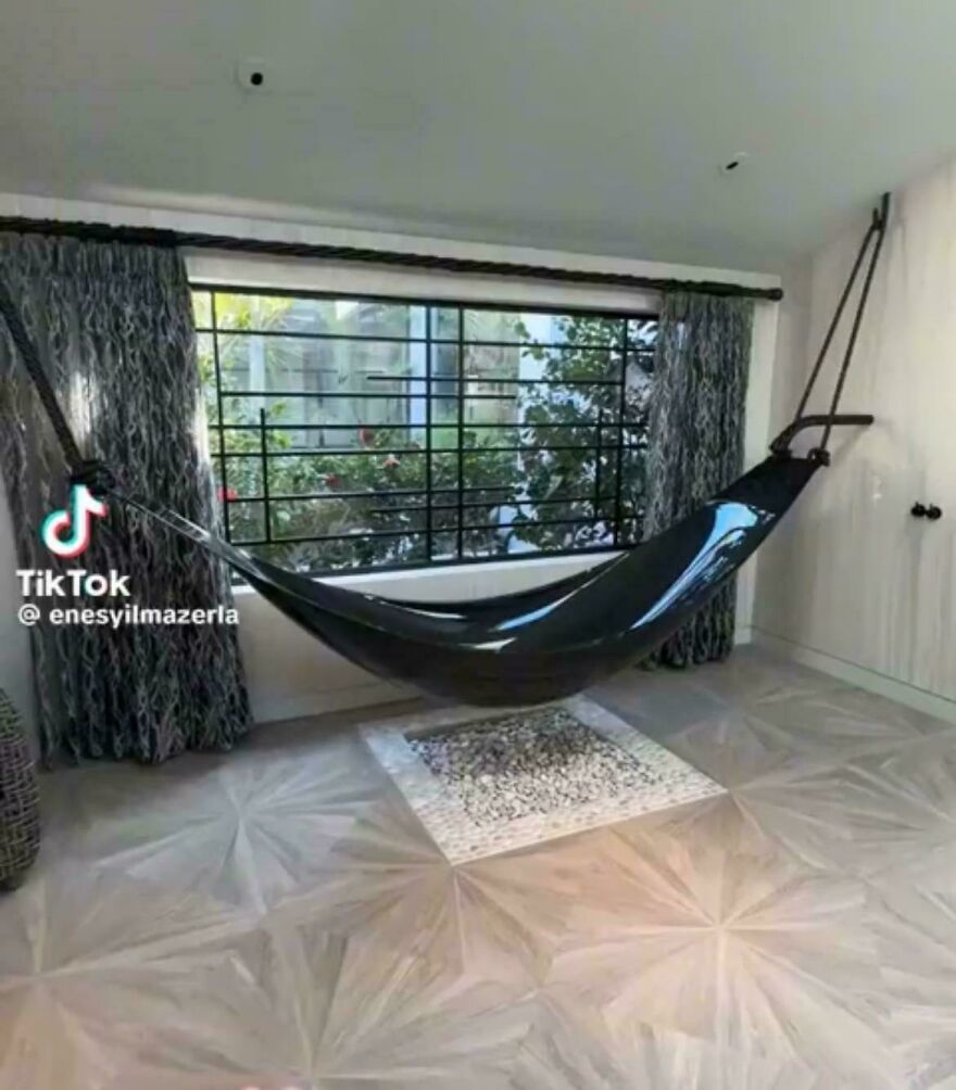 Glossy black hammock installed indoors over a decorative stone floor, showcasing designers going too far with impossible to use design.