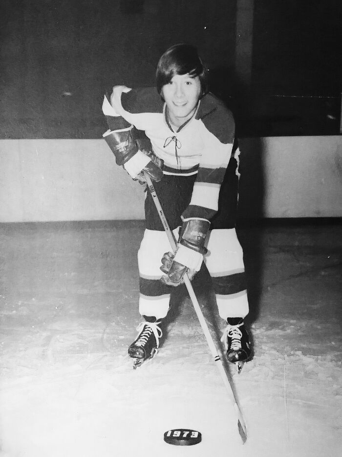 Black and white childhood photo of a boy in hockey gear posing on ice with a stick and puck from 1979.
