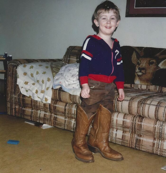 Child wearing oversized cowboy boots standing in living room, a funny and awkward childhood moment shared online.