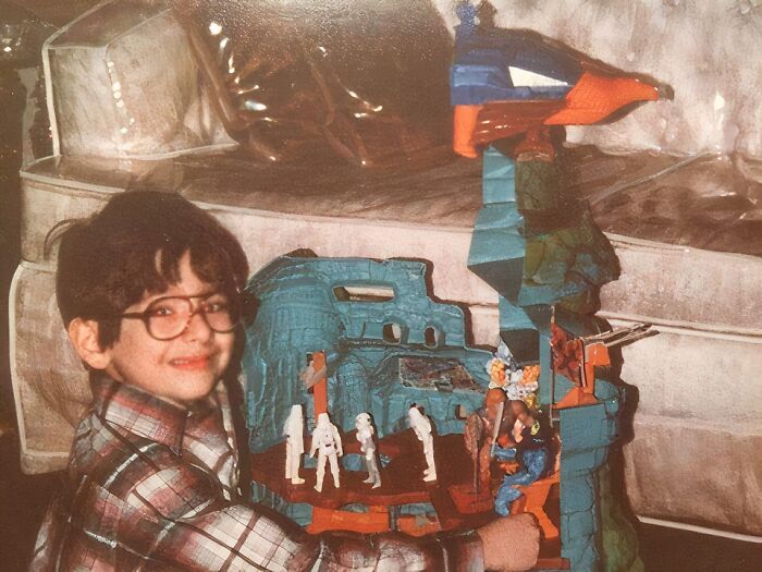 Child holding a vintage toy castle, smiling awkwardly in a hilariously awkward childhood pic from a retro family photo.