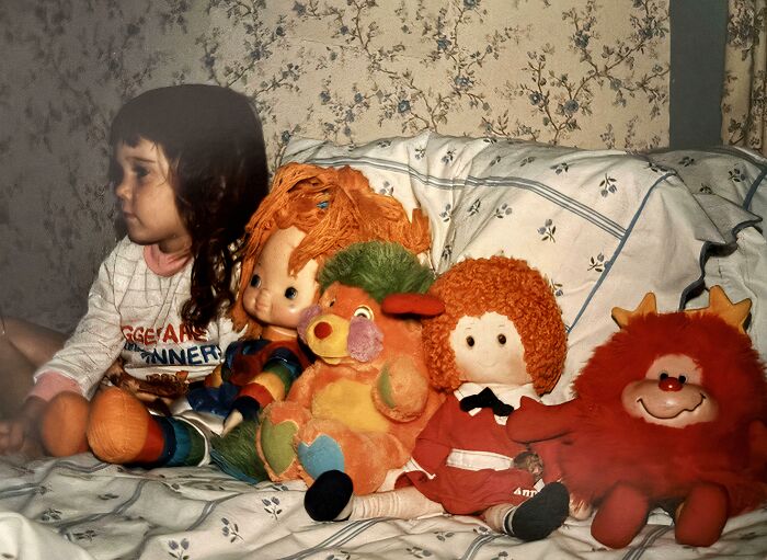 Child sitting on bed with vintage colorful toys, capturing a hilariously awkward childhood moment in a nostalgic setting.