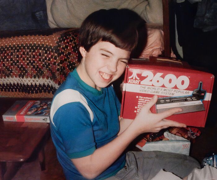 Child holding an Atari 2600 video game system, captured in a funny and awkward childhood moment.