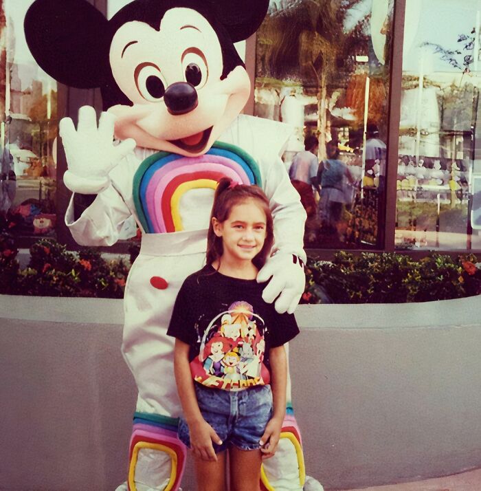 Girl standing awkwardly with colorful Mickey Mouse character costume, a hilariously awkward childhood pic shared by people.