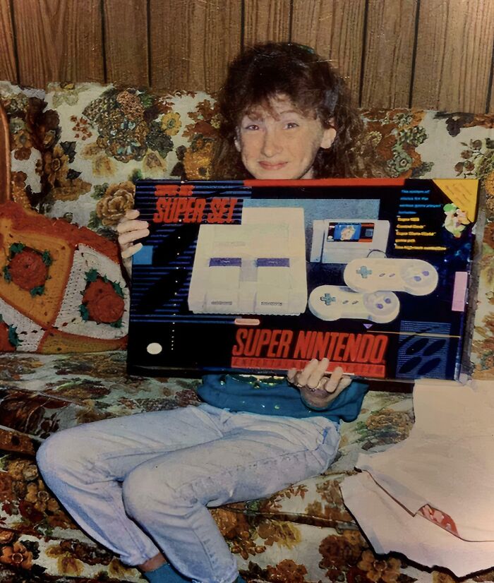 Child holding a boxed Super Nintendo on a floral couch, a classic childhood moment in hilariously awkward childhood pics.